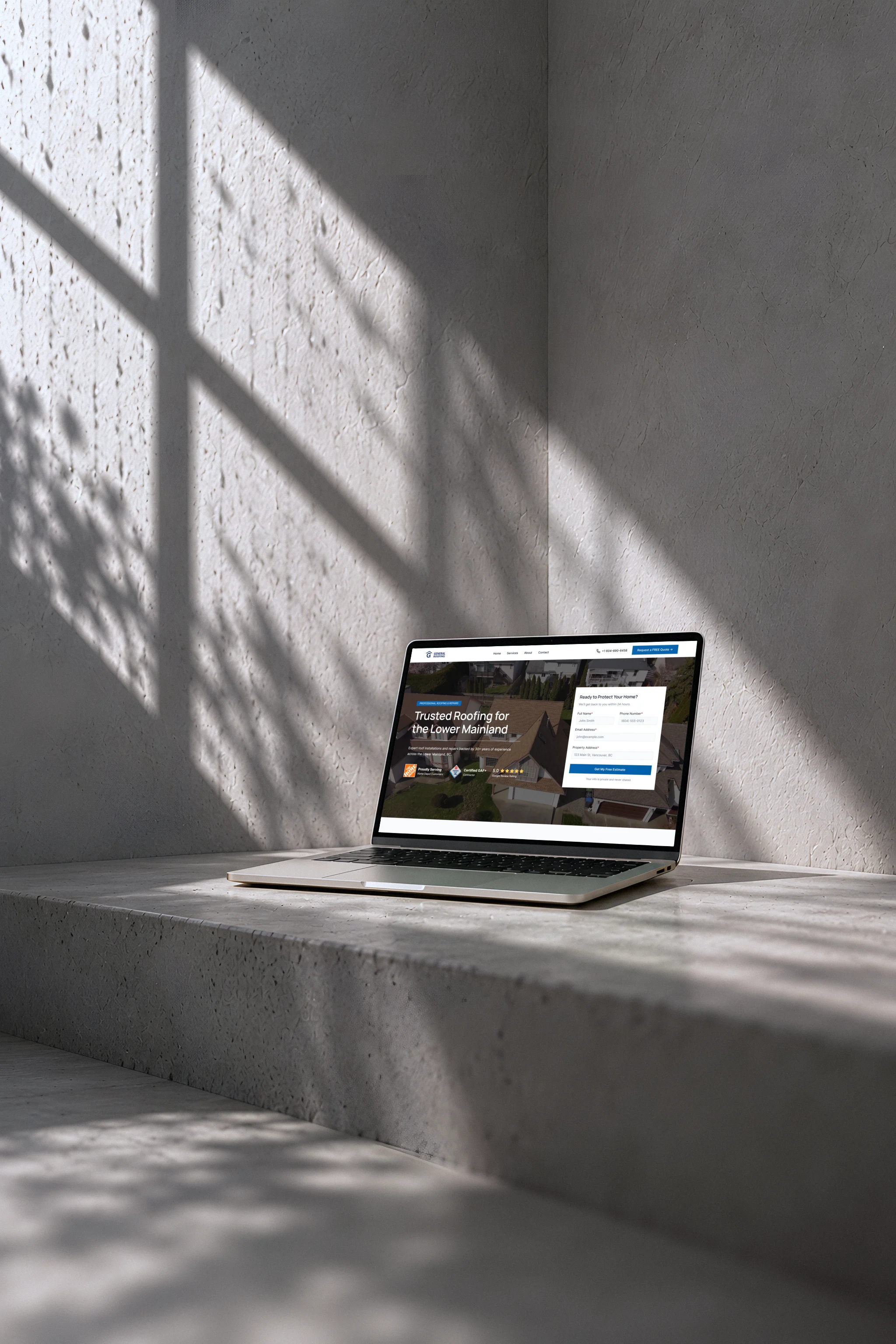 General Roofing’s homepage on a laptop on a low concrete step in the corner of two plaster walls, a shaft of rainy window light across them